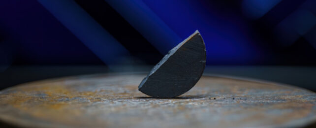 Semi-circular piece of material resting on its side edge on grey surface in front of blue lights.